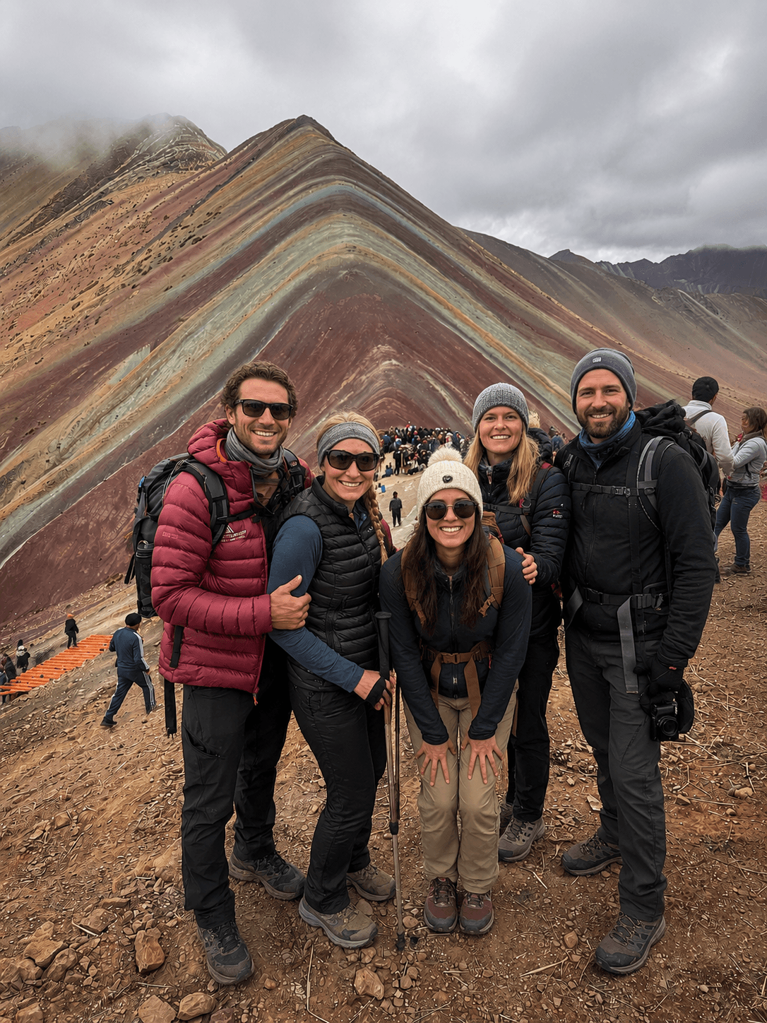 Cinco viajeros posando frente a las coloridas laderas de Vinicunca en los Andes peruanos.