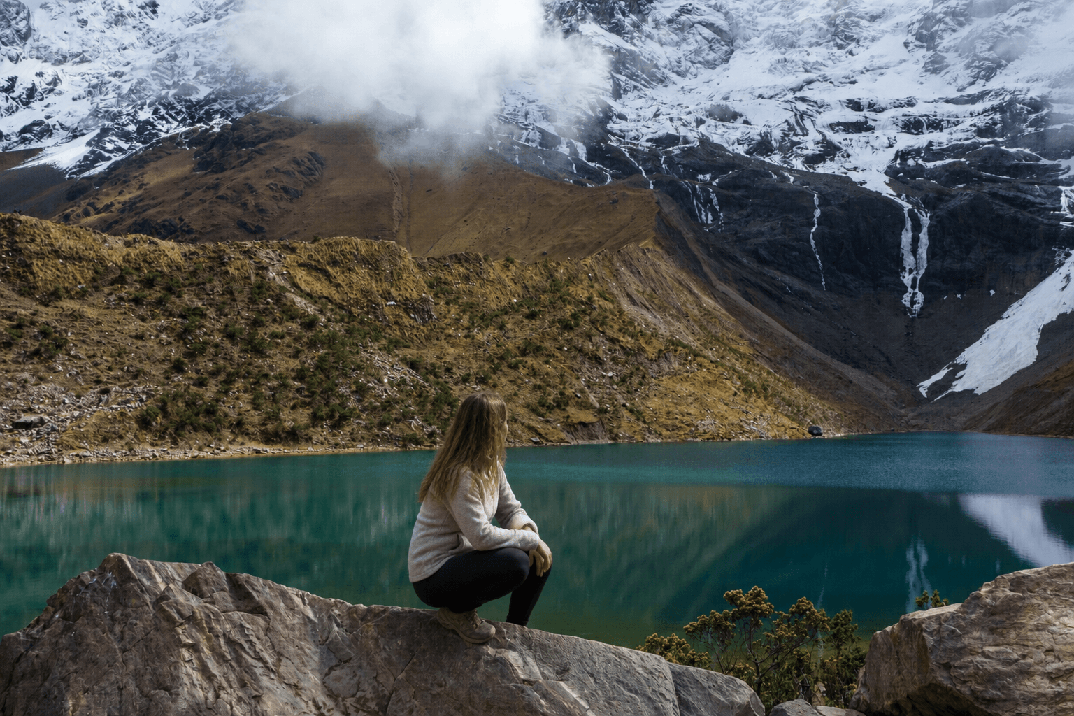 Travelers overlooking the turquoise waters of Humantay Lake below snow-covered Andean peaks.